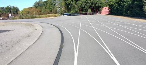 Le marquage blanc encore net sur l'enrobé, au départ de la ligne droite ; à gauche, le caniveau à grille qui borde la corde — Complexe Sportif de Bellestre, Bouaye