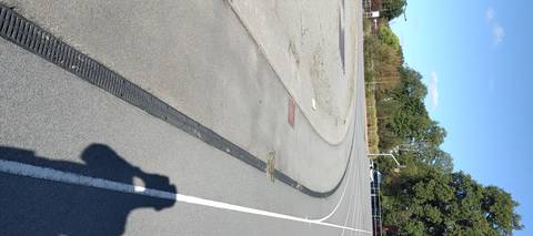 Le caniveau à grille suit la corde sur tout l'anneau ; à gauche, le terre-plein central réduit à une aire de gravier — Complexe Sportif de Bellestre, Bouaye