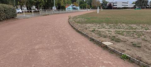 L'anneau en cendrée dans un virage, bordé de vieux béton ; au centre le terrain engazonné et ses poteaux de rugby — Complexe Sportif de la Croix Jeannette, Bouguenais
