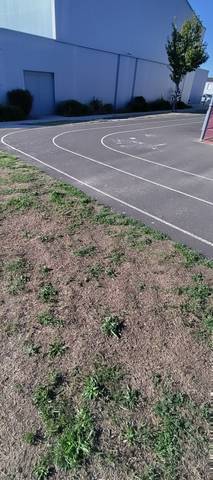 Un virage : l'enrobé sombre et ses lignes blanches, le changement de direction très marqué, le pignon du complexe sportif au fond et le grillage rouge du city-stade à droite — Complexe Sportif, La Limouzinière