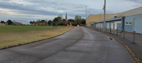 Le virage bordé par le gymnase, bancs le long de la piste, terrain de football en herbe au centre et clocher du bourg en fond — Complexe Sportif Gauvrit, Sainte-Pazanne