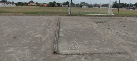 L'aire de lancer du poids : dalle béton fissurée, cercle à peine lisible, terrain de football en fond — Complexe Sportif du Parc du Grand Fay, Saint-Père-en-Retz