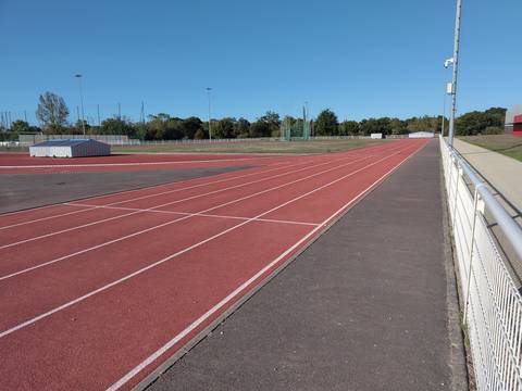La ligne droite en tartan vue depuis la main courante ; au fond, la cage de lancer et les matelas de saut bâchés — Stade Muriel Hurtis — Complexe des Chevrets, Saint-Philbert-de-Grand-Lieu