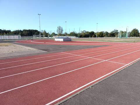 L'anneau de 250 m et son virage ; à droite, la cage grillagée du marteau et du disque en bord de terre-plein — Stade Muriel Hurtis — Complexe des Chevrets, Saint-Philbert-de-Grand-Lieu