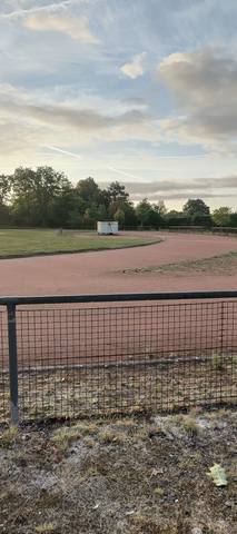 Un virage et la pelouse centrale : la cendrée rejoint l'herbe sans lice ni bordure, une cabane blanche posée en bord de piste — Complexe sportif de la Cailletière, Challans