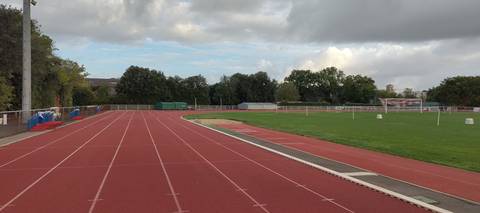 La ligne droite : marquage net sur tartan rouge, matériel rangé le long de la main courante à gauche, sautoir et pelouse à droite — Complexe sportif Jean Léveillé, Challans