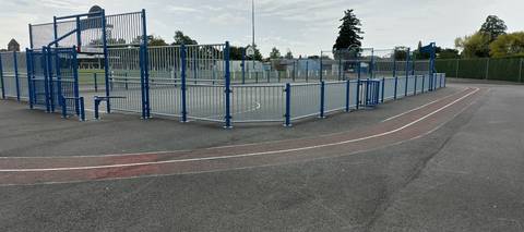 Le virage : deux couloirs lignés de blanc sur l'enrobé, le couloir 1 peint en rouge, autour du city-stade aux barrières bleues — Gymnase du Moulin Bleu, Montbert
