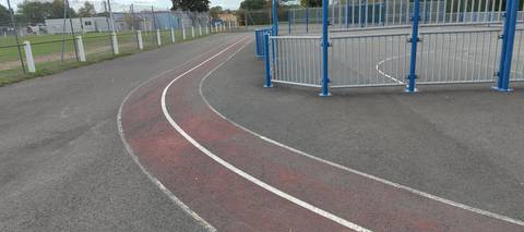 Le virage serré entre le city-stade et le terrain de football grillagé, la peinture rouge du couloir 1 usée par endroits — Gymnase du Moulin Bleu, Montbert