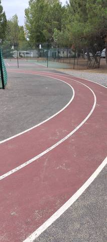 Le virage : marquage blanc net sur enrobé coloré, court de tennis à gauche et mobil-homes du village de vacances en fond — Piste du Domaine du Collet (Les Moutiers-en-Retz), Les Moutiers-en-Retz